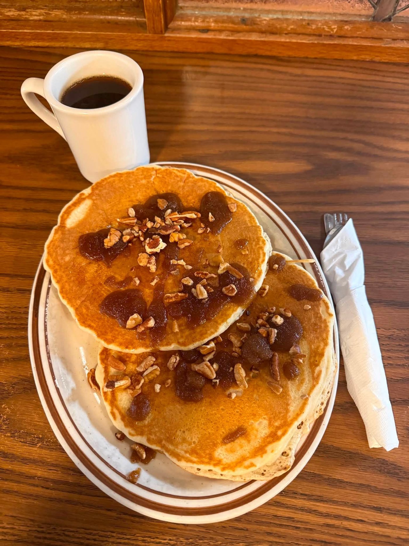 Two pecan pancakes with apple butter and chopped pecans, with a mug of coffee